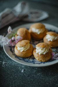 Delicious choux buns with cream on an elegant floral plate adorned with blossoms.