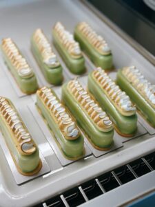 Freshly baked green pistachio eclairs with decorative icing on a tray.